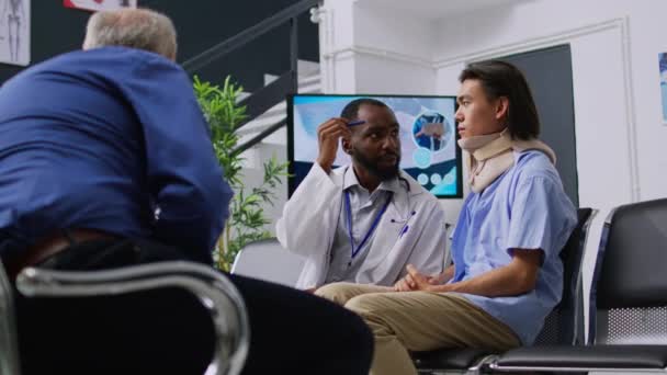 アフリカ系アメリカ人医師が脳損傷検査を行い 脳震盪をチェックし 患者と医療相談を行う 待合室で首の骨折をした者 — ストック動画