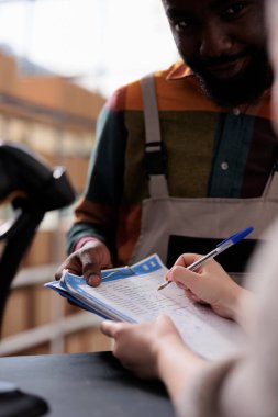 Yönetici ürünleri imzalar, paketleri hazırlamaya başlamadan önce müşterileri çevrimiçi olarak tartışır. Çeşitli çalışanlar depodaki mal denetim listesini inceliyor. Kapat.