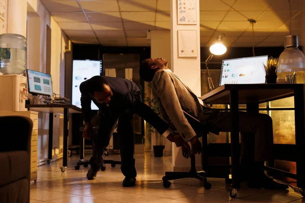 매니저는 사무소에서 잠이든 의자를 꺼내고 아프리카 미국인 직원들은 통계를 분석하는 — 스톡 사진