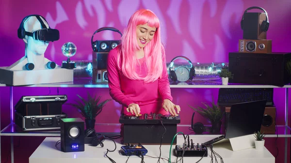 Djテーブルダンスでピンクの髪の立っているミュージシャンや電子機器とステレオサウンドを混合しながら 楽しみを持っています ナイトクラブでプロのミキサーコンソールを使用して音楽を演奏することを楽しむ笑顔アーティスト — ストック写真