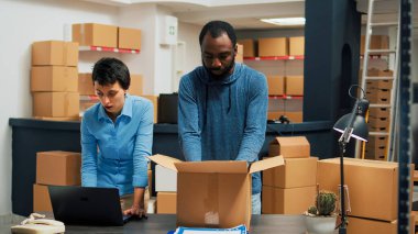 Business owners giving highfive after putting products in cardboard boxes, finishing quality control and delivery logistics. Man and woman feeling cheerful about merchandise distribution.