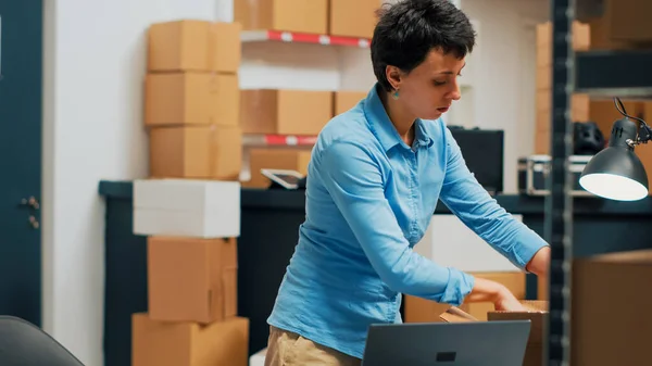 Young adult using merchandise from warehouse to prepare order, shipping products before doing inventory. Female employee planning distribution management, woking on business development.