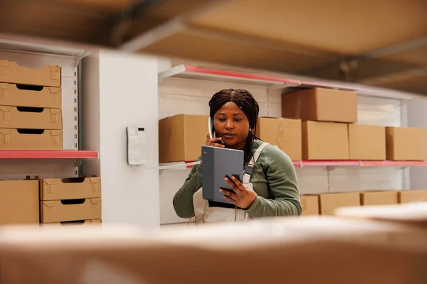 非洲裔美国人工人通过固定电话与远程经理交谈 讨论仓库中的产品库存 在平板电脑上全面检查网上订单的员工 — 图库照片