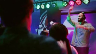 Dans partisinde karaoke yapan mutlu kadın, sahnede DJ ile DJ karışık şarkılar söyleyen. Neşeli insanlar dans ediyor, sosyal toplantılarda eğleniyorlar, eğleniyorlar. El kamerasıyla..