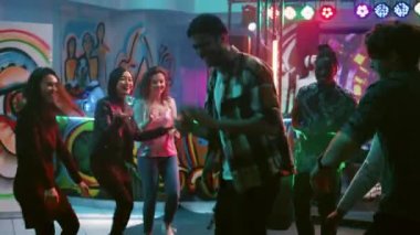 Genç yetişkinler eğleniyor, dans ediyor ve dans pistinde sahne ışıklarıyla dolaşıyorlar. Eğlenceli dans hareketleri yapan neşeli arkadaşlar yeraltı partisinde eğleniyorlar. El kamerasıyla..