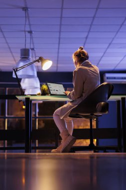 Yönetici yönetici dizüstü bilgisayarında masa başında oturmuş şirket istatistiklerini analiz ediyor. Şirket çalışanı gece geç saatlere kadar çalışıyor.