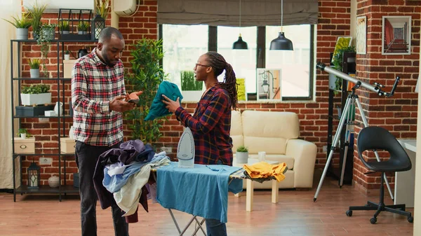 Tired Modern Wife Ironing Laundered Clothes While Relaxed Husband Uses — Stockfoto