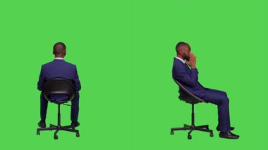 Genç işadamı sandalyede oturuyor ve bekliyor, resmi ofis elbisesi giyiyor ve yeşil perde arkasında poz veriyor. Erkek girişimci stüdyoda iyimser, şık bir işçi..