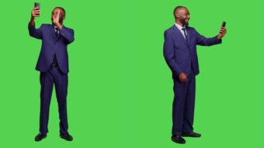 Erkek girişimci akıllı telefondaki video konferans web kamerasında el sallıyor, tüm vücut yeşil ekranında internet telekonferans sohbetini kullanıyor. Video konferansına katılan genç işadamı.