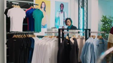 Kadın müşteri elbise koleksiyonunu inceliyor ve mağazadaki kumaşları kontrol ediyor. Genç Alışverişçi, perakende pazarından günlük ya da resmi kıyafet almak istiyor. Üçayak atışı.