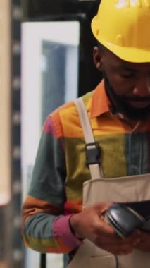 Dikey video: Depodaki raflarda malları tarayan genç çalışanlar, tarayıcı ve tabletle ticaret dağıtımı için çalışıyorlar. Depo çalışanı teslimattan önce ürün envanterini kontrol ediyor..
