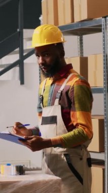 Dikey video: Teslimat ekibi depo alanında malzeme topluyor, ürün ve üretim üzerinde çalışıyor. Genç adam ve kadın kargo siparişlerini, envanter listesini kontrol ediyorlar..