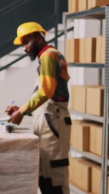 Dikey video: Depo amiri teslimat listesini imzalıyor, malları kutular içinde nakliyeye hazırlıyor. Perakende satış mağazası taşımacılığında çalışan çeşitli çalışanlar, depolama odasındaki ürünleri kontrol ediyorlar..