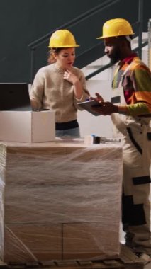 Dikey video: Depolama odasındaki ürünleri inceleyen iki işçi, sevkiyattan önce bilgisayardaki ürün listesini gözden geçiriyorlar. Tedarik zinciri yönetimi ve kalite kontrolü üzerine çalışan genç bir ekip.