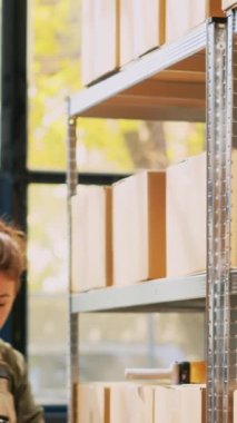 Dikey video: Denetmen raflardaki barkodları tarıyor, kargo denetimi ve depoda doğrulama üzerinde çalışıyor. Ürün kutularının incelenmesi ve envanter listesinin kontrol edilmesi, sipariş teslimatının hazırlanması