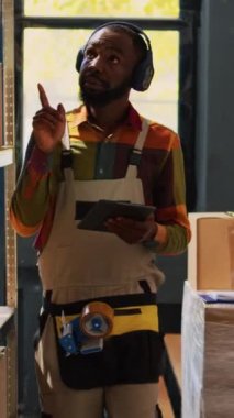 Dikey video: Kaygısız yetişkin envanterle eğleniyor, ambarda müzik dinlerken raflarda merhcandise analiz ediyor. Genç işçi kargo stoklarına bakıyor, raflar arasında dans ediyor..