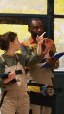Dikey video: Depo çalışanları mağaza siparişlerini hazırlamak için malzeme lojistik ve tablet listesini kullanarak ambardaki ürünleri inceliyorlar. Ekip çalışanları kargo stoklarını inceliyor..