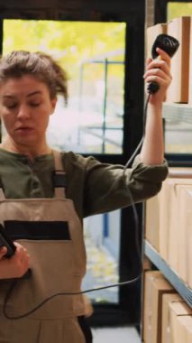 Dikey video: Depo envanteri için tablet tarayıcı kullanarak barkodları tarayan stok odası çalışanı, ürünleri kontrol ediyor. Kadın işçi, hisse senedi lojistiği, depo teftişi....