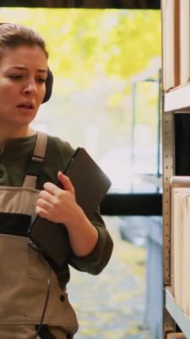 Dikey video: Depo çalışanı müzik dinliyor, raflar ve raflar arasındaki ticari barkodları tarıyor. Kadın denetçi ürün stoklarını gözden geçiriyor ve depoda dans ediyor.