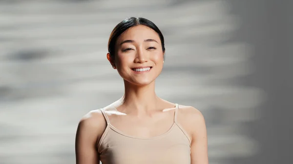 Beautiful person creating skincare cosmetics ad, posing with glamour and tenderness on camera. Asian woman promoting beauty products for radiant luminous skin, body acceptance.