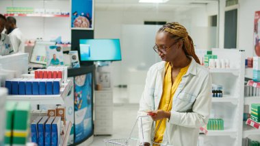 Female customer taking pills and medicine from shelves, looking at medicaments and packages of drugs. Young adult checking pharmaceutics for healthcare treatment, pharmacy shop.