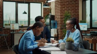 Şirket çalışanları brifing ofisindeki belgeleri inceliyor, şirket bilgileriyle evrakları inceliyor. Birlikte çalışma alanında yeni şirket vizyonu üzerinde çalışan Afrikalı Amerikalılar.