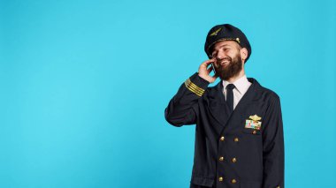 Male aviator talking on smartphone call and laughing, feeling positive and having remote conversation. Young cabin pilot wearing flying uniform for commercial flights, telephone line.