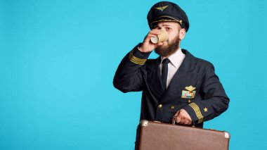 Aircrew captain carrying suitcase baggae at work, preparing for commercial flight in studio. Young pilot with flying aviation uniform holding briefcase and working on air transportation.