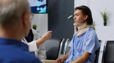 Boyunluk takan Asyalı hasta yaşlı doktorla görüşüyor, görme ve beyin hasarını ışıkla kontrol etmek için beyin sarsıntısı muayenesi yapıyor. Sıhhiye ile sağlık kontrolüne katılan kişi.