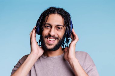 Neşeli yüzlü Arap adam kulaklıkla müzik dinliyor. Neşeli gülen insan, kaygısız ve keyifli bir şekilde kameraya bakarken müzik listesinden zevk alıyor.