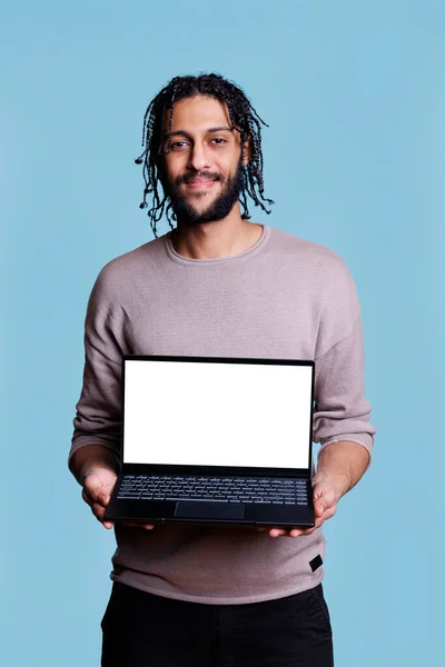 微笑的Arab男人拿着白色空白屏幕的笔记本电脑进行营销演示 模仿和看着相机 显示用于计算机软件的带有空显示的便携式设备的人 — 图库照片