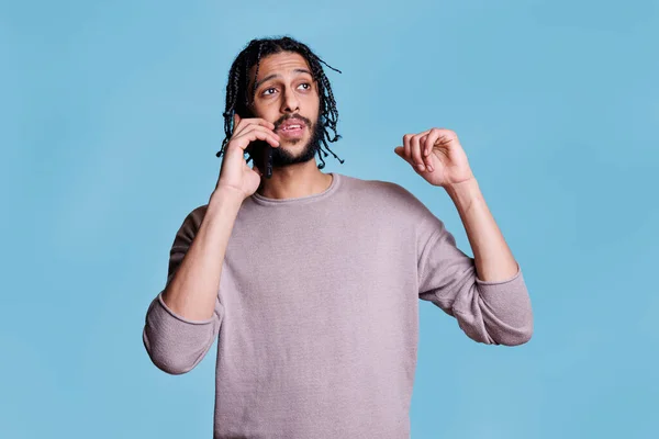 Young arab man chatting on mobile phone while explaining thoughts and gesticulating with hands. Handsome person in casual clothes answering call, having conversation on smartphone