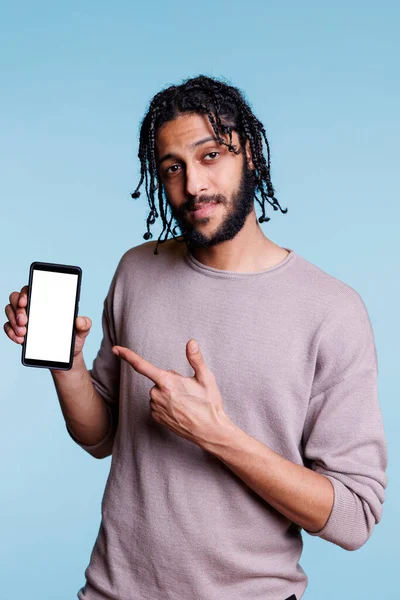 自信的广告主拿着智能手机 一边看着相机一边指着白色的空触摸屏 男人用空白显示展示手机 做广告产品 — 图库照片