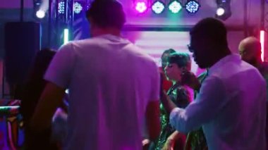 Genç yetişkinler etkinlikte birlikte parti yapıyorlar. Funk müzik dinliyorlar, dans pistinde eğleniyorlar. Neşeli insanlar disko partisinde DJ ve spot ışıklarıyla, canlı performansla eğleniyorlar. El kamerasıyla..