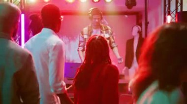 DJ adam sahnede ses istasyonunu kullanıyor, diskotekte bir grup insanla parti yapıyor. Müzik setinde müzik çalan, gece kulübünde eğlenen, dans eden ve zıplayan eğlenceli yetişkinler. El kamerasıyla..