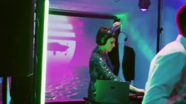 Genç yetişkin, partide müzik çalıyor, arkadaşlarıyla diskotekte DJ olarak çalışıyor. Sahnede disko ışıklarıyla ses karıştırma istasyonunu kullanan bir kadın, bir grup insanla eğleniyor. El kamerasıyla..