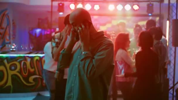 在夜总会接电话的人 在迪斯科舞会上试着进行远距离交谈 男人在智能手机上聊天 享受夜晚的活动与时髦的音乐 手持射击 — 图库视频影像