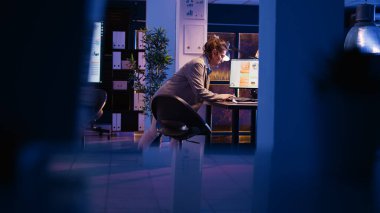 Cheerful manager planning financial report in office and analyzing economy diagrams overtime. Young advisor checking analytics on computers, working on business project. Handheld shot.