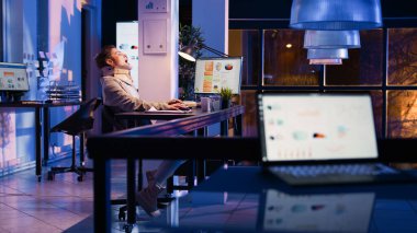 Sick employee in cervical collar working late at night, suffering from neck pain in corporate office. Startup worker trying to finish financial report, business solutions. Handheld shot.