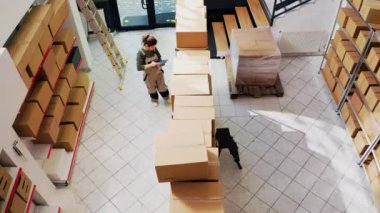 Teslimat ekibi depo ürünlerini kontrol ediyor. Malzemeleri ve kargoyu bilgisayarlı kutularda inceliyor. Kadın ve erkek perakende satış ürünleri üretimini onaylıyor. İHA atışı. Üst görünüm.