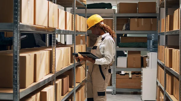 非洲裔美国妇女手持平板电脑扫描条形码进行库存工作 使用扫描仪和对仓库商品进行分类 仓库工人检查货架上的纸板箱 — 图库照片