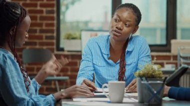 Analiz raporları hazırlayan iş arkadaşları, başlangıç ofisinde kalkınma için iş çözümlerini gözden geçirmek üzere toplanıyorlar. Birlikte çalışma alanında yeni kar artırımı stratejisi tartışan bir grup insan. El kamerasıyla..