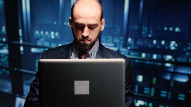 System administrator checking cluster computer service holding laptop in modern server room. Data center technician analyzing backup digitalization for networking industry. Handheld shot.