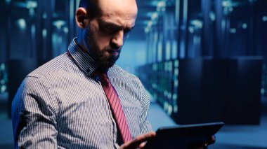 Veri merkezi bilişim mühendisi sunucu dolaplarının yanında duruyor, dijital tablette donanım sunucu sistemini etkinleştiriyor. Yüksek teknoloji sunucu odasında veri tabanı bilgileriyle çalışan bir bilişim yöneticisiyim. El kamerasıyla..