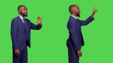 Stüdyoda birine el sallayan genç bir işadamı yeşil perde arkasında bir şey düşürdüğünü söylüyor. Erkek şirket çalışanı yeşil ekranı işaret ediyor..