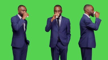 Stüdyoda kahve fincanının keyfini çıkaran erkek ofis çalışanı yeşil perde arkasında duruyor. İş adamı kendinden emin ve pozitif. Kamerada kafein içeceği, izole edilmiş bir model..