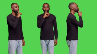 Gizlilik jestini parmaklarıyla yapan, mahremiyetini ifade eden ve bazı şeyleri gizli tutan özel bir kişi. Genç yetişkin, yeşil ekran arkaplanı üzerinde sessiz sessizlik işareti yapıyor..