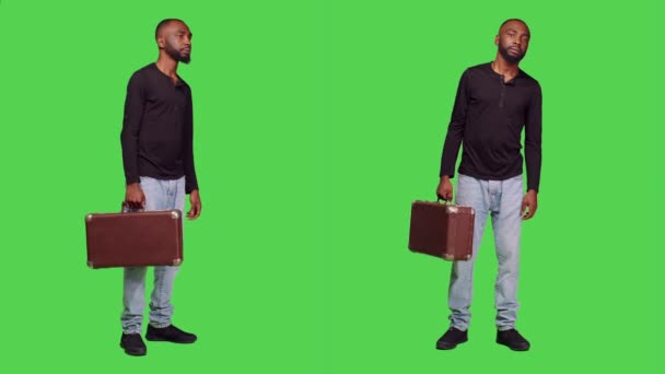 カメラにスーツケースの荷物を抱えて何かを待っているカジュアルな人は 緑の画面の背景の上に立っている 若いです男でブリーフケースを運ぶ荷物でスタジオ 優しい大人 — ストック動画