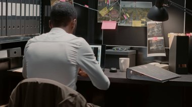Police investigator working on criminal case in incident room, reading witness statements. Young law officer analyzing archive files, doing research with suspicious photos in office.