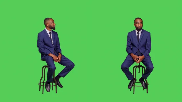 スタジオの椅子に座って 何かを探して待っているスタートアップの従業員を自信を持って 緑の画面の背景に正式なビジネススーツを着て若い経営者 — ストック写真